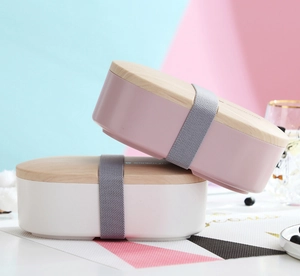 Detail of minimalist oval lunch box with wood-style lid and elastic strap in pastel colors