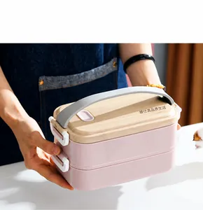 Pink double-layer bento box with wood grain lid and carry handle shown in a hand-held view