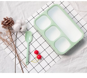 Detailed view of light green four-compartment bento box with matching spoon and dividers