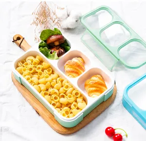 Detailed top view of mint green three-compartment lunch box with clear lid on wooden tray