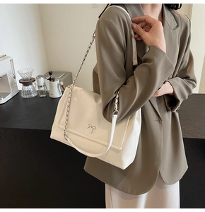 Close-up of cream white shoulder bag featuring a silver bow detail and chain strap