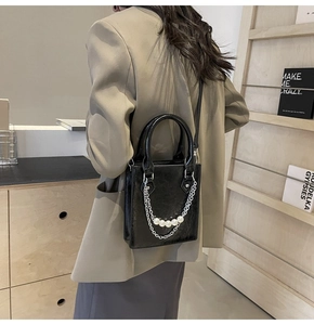 Détail du sac bandoulière noir avec chaîne argentée et perles porté par le mannequin
