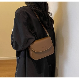 Dettaglio borsa a tracolla in pelle marrone scuro con fibbia dorata su modella