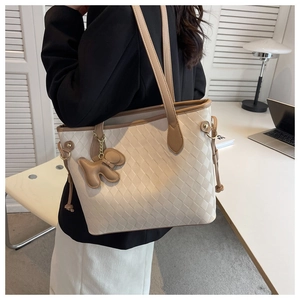 Détail d'un grand sac cabas matelassé beige avec bordure marron et breloque chiot
