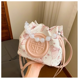 Detail of beaded handle on beige canvas bucket bag with pink butterfly prints