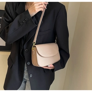 Dettaglio di una borsa a tracolla beige minimalista con finiture dorate su una modella