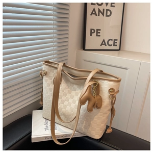 Détail du sac cabas à damier avec lanières en cuir et breloque chien doux sur un canapé