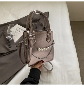 Détail d'un sac argenté métallisé avec chaîne perlée et texture plissée sur lit blanc