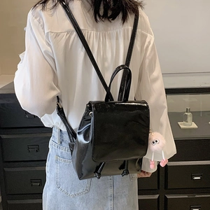 Glossy black patent leather mini backpack with a pink plush charm on a female model