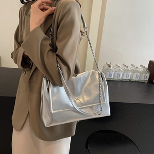 Silver soft leather tote bag with bow buckle and chain strap shown on model's shoulder