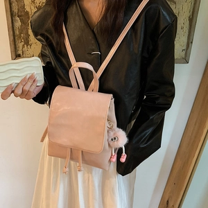 Pink mini faux leather backpack with plush monster keychain worn by model