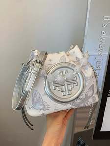 White bucket bag with butterfly prints, beaded handle, and silver geometric ornament