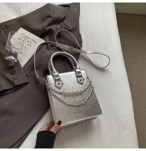 Détail d'un sac argenté texturé avec chaîne en perles et bandoulière réglable