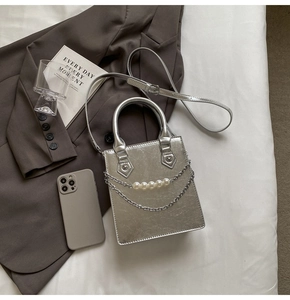 Sac à main carré argenté avec détails de perles et chaîne sur fond de veste texturée