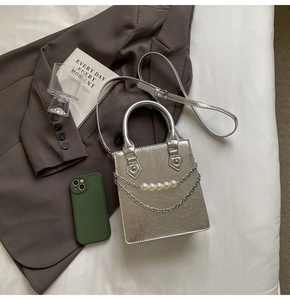 Détail du sac à main argenté avec chaîne de perles et fini métallisé sur drap blanc