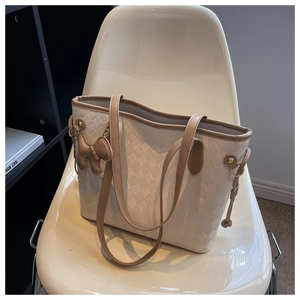 Détail d'un sac cabas beige matelassé avec bordure en cuir brun et breloque chiot