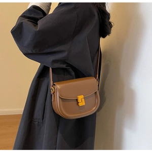 Dettaglio di una borsa a sella marrone in pelle con una chiusura girevole rettangolare dorata