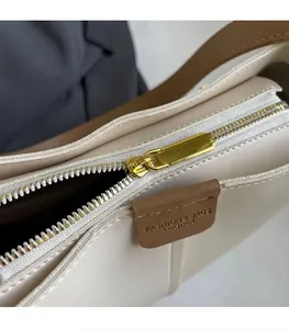 Close-up of smooth metal zipper and leather tag on a minimalist beige crossbody bag
