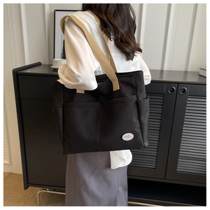 Detail einer schwarzen Canvas-Tasche mit beigen Henkeln und vorderen Taschen