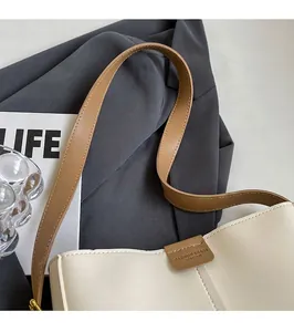 Close-up of minimalist cream leather bag with brown embossed logo tag and shoulder strap