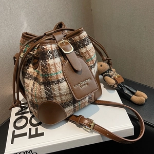 Retro tweed and leather bucket bag with a cute bear charm on a fashion book background