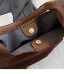 Detail of the magnetic buckle closure and suede texture on this dark brown tote bag