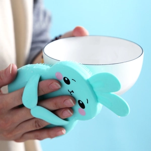 Mint green bunny silicone cleaning brush with soft bristles washing a ceramic bowl