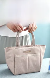 Detail of a beige thermal lunch bag featuring a double handle and front pocket compartments