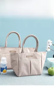 Detailed view of beige canvas lunch bag set with brown leather tag and front pocket