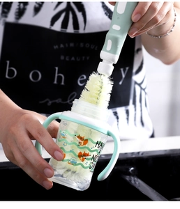 Detail showing a long-handled cleaning brush washing a cartoon baby bottle with soft bristles