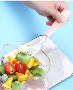 Pink handle stainless steel fruit fork picking fresh kiwi from a stylish glass bowl
