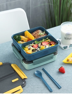 Close-up of dual-layer lunch box with leak-proof seals and utensils on a dining table