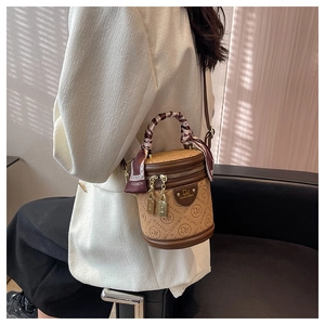 Detail der braunen Eimertasche mit Monogramm-Prägung und Seidentuch am Griff