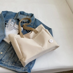 Nahaufnahme der cremefarbenen Canvas-Tasche mit braunen Trägern und Good Luck Abzeichen