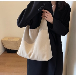 Detail of a large cream suede tote bag styled with a black blazer for daily commute