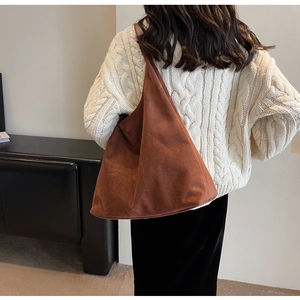 Close-up of brown suede hobo bag with wide shoulder strap worn by a model in a knit sweater