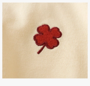 Close-up of red four-leaf clover embroidery on soft beige cotton knitted fabric