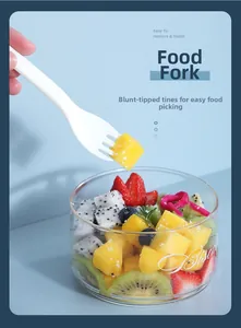 Detail of portable food fork with blunt teeth picking mango from a fruit glass bowl