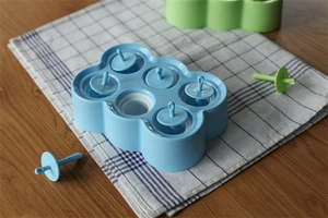 Detalle de molde azul para polos de 6 cavidades con mangos antigoteo sobre mantel de cuadros