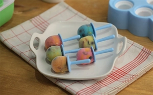 Mini helados de colores en plato de cerámica blanca con palos de plástico azul