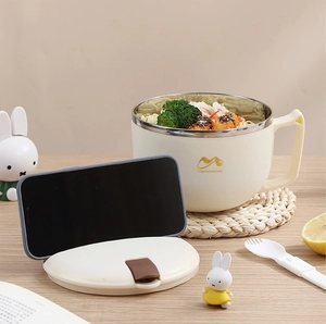 Detail of beige stainless steel noodle bowl with phone holder lid on a warm desk setup