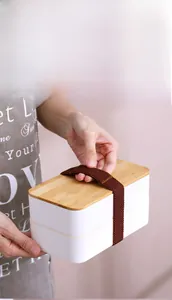 Close-up of double-layer lunch box with natural bamboo lid and elastic strap detail