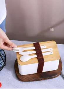 Detail of a white double-layer lunch box with a bamboo lid and elastic band including cutlery