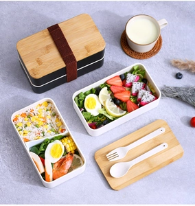 Detail of double-layer lunch box with bamboo lid, elastic strap, and utensils on marble table