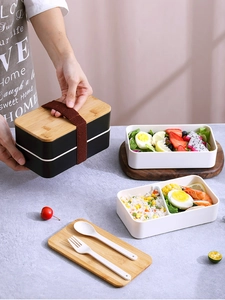 Close-up of double-layer lunch box with bamboo lid, elastic strap and cutlery set