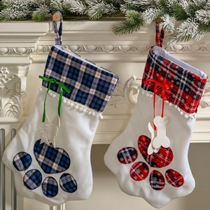 Red and blue plaid pet Christmas stockings with paw prints hanging by a white fireplace