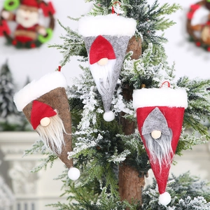 Tres colgantes de gnomos navideños en rojo, gris y marrón colgados en un árbol nevado