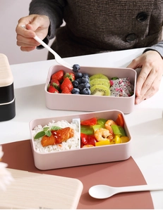 Dettaglio del bento box rosa impilabile con frutta fresca, riso e piatti di mare