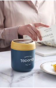 Close-up of portable stainless steel soup cup with yellow lid on a marble tabletop
