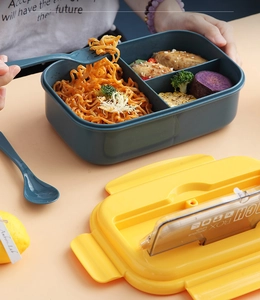 Three-compartment bento lunch box with utensils shown in a dynamic meal serving scene